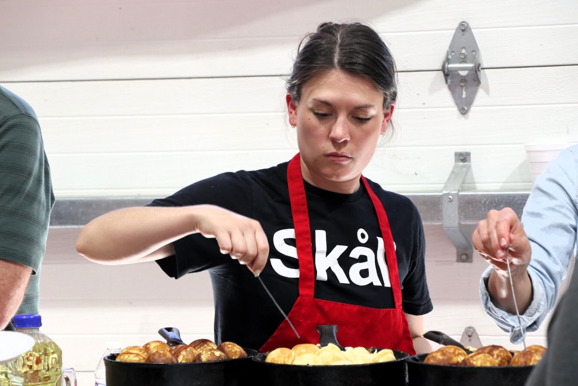 A woman wearing a skål shirt and apron prepares æbleskiver.