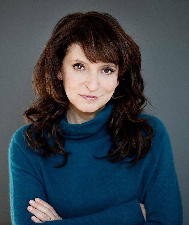 Dressed in a blue turtleneck, Susanne Bier poses for a headshot with her arms crossed.