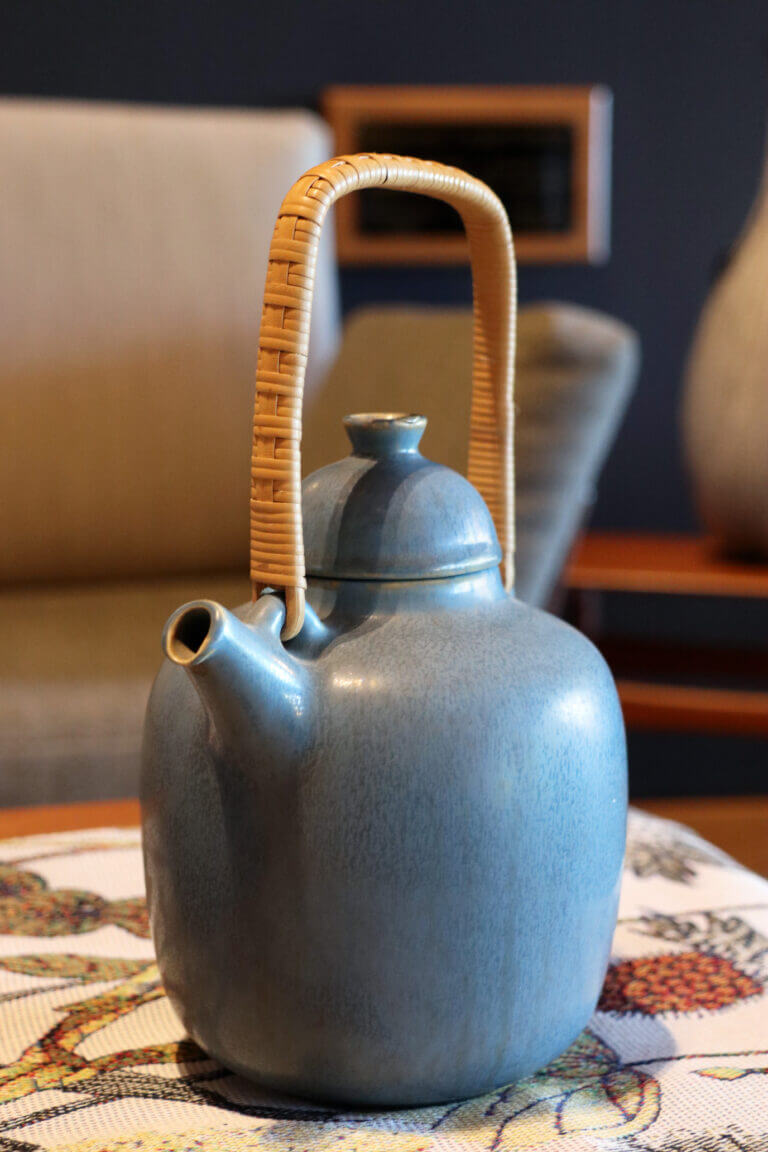 A blue glazed Palshus teapot resting on a coffee table.