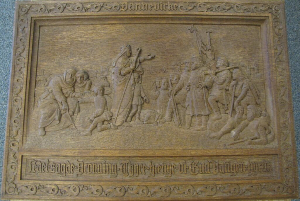 a wooden carving of a woman standing in front of a crowd of men
