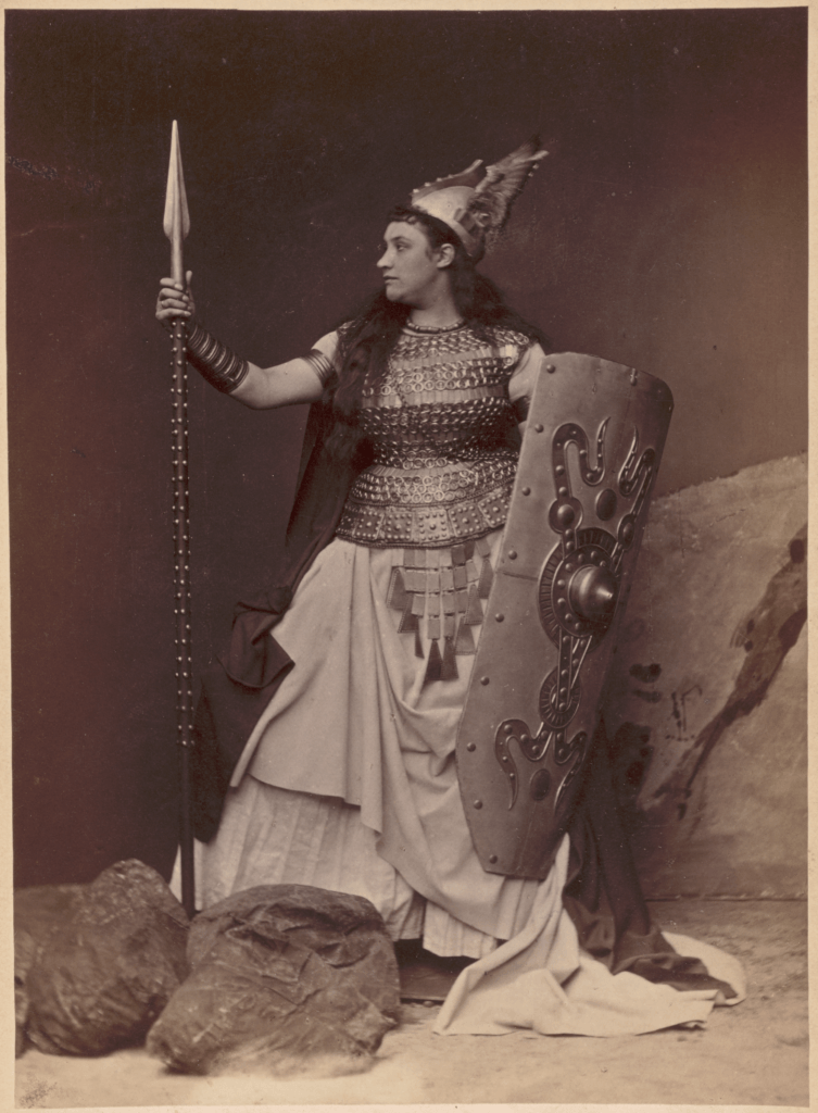 A women looking left, holding a spear and a shield.