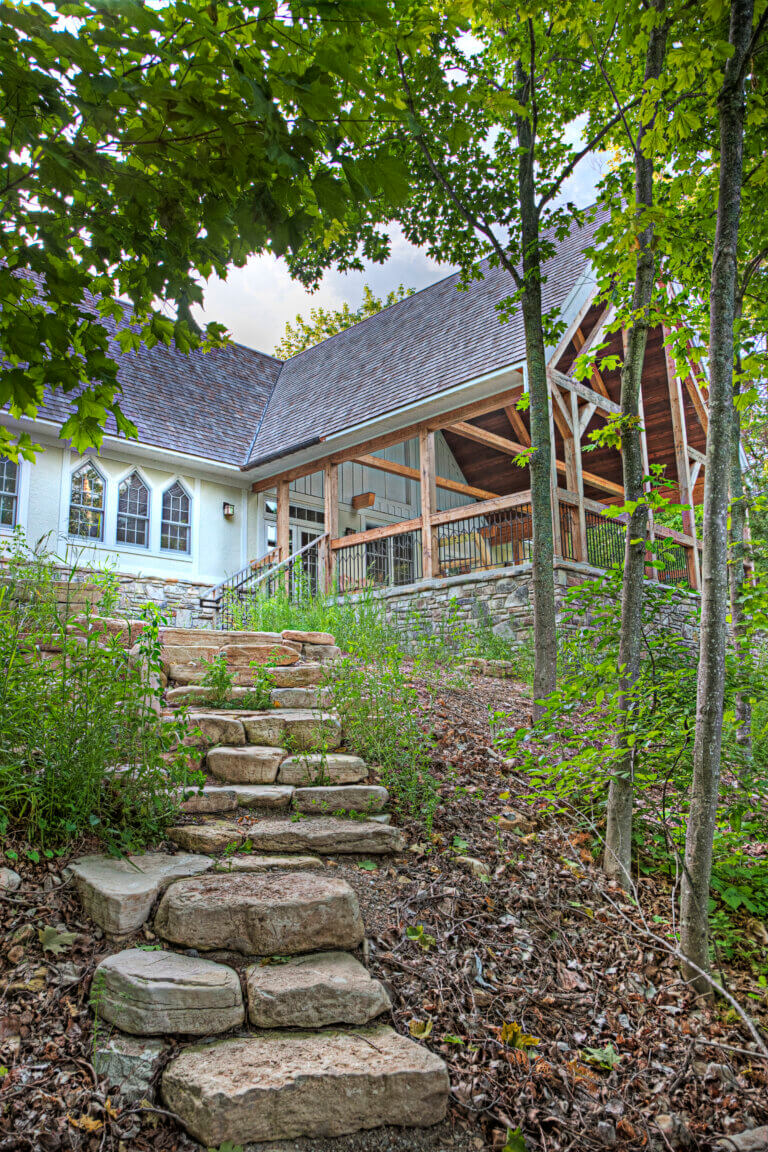a view of a white building. Stone stairs head from the building to the bottom left of the image. trees grow on the right.