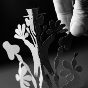 A paper cut figure, the figure has a hat its hands raised, besides it are mushrooms.