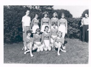 Ten women are in the center, nine of them are wearing a gymnast uniform consisting of a skirt and long sleeved top.