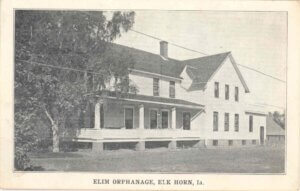 Black and white photo postcard of Elim Orphanage in Elk Horn, IA. Building is white with a dark roof.