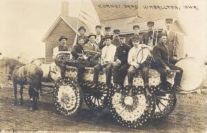 A band sits on a horse drawn wagon, the wagon is decorated with stars and stripes banners.