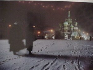 A snow covered ground with many footsteps two people are to the left, in the background is Saint Basil's Cathedral