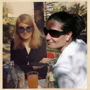 Two women both with sunglasses on are sitting at a table