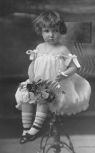 A girl sitting on a chair, she is in a white dress and holding flowers