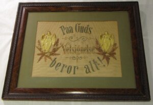 Framed artwork with ornate text reading "Paa Guds Velsignelse beror alt!" flanked by two angels on a beige background,