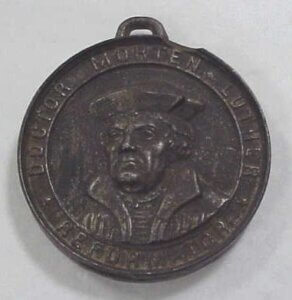 Metal medallion featuring a man's head. Around the edge of the medallion is text reading "Doctor Morten Luther. Reformator."