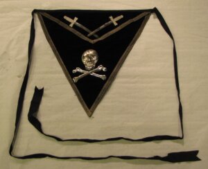 Black apron featuring a silver skull and bones. at the top of the apron are two crossed swords.