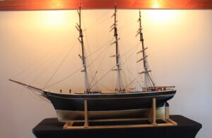 Model of a sailing ship with three masts, The ship has a black hull and a natural wood underside.