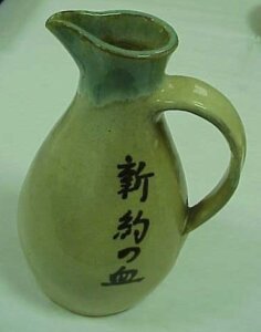 A green ceramic pitcher with black Japanese signs down the side.