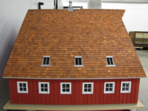 Model of a red barn with an orange-brown shingled roof.