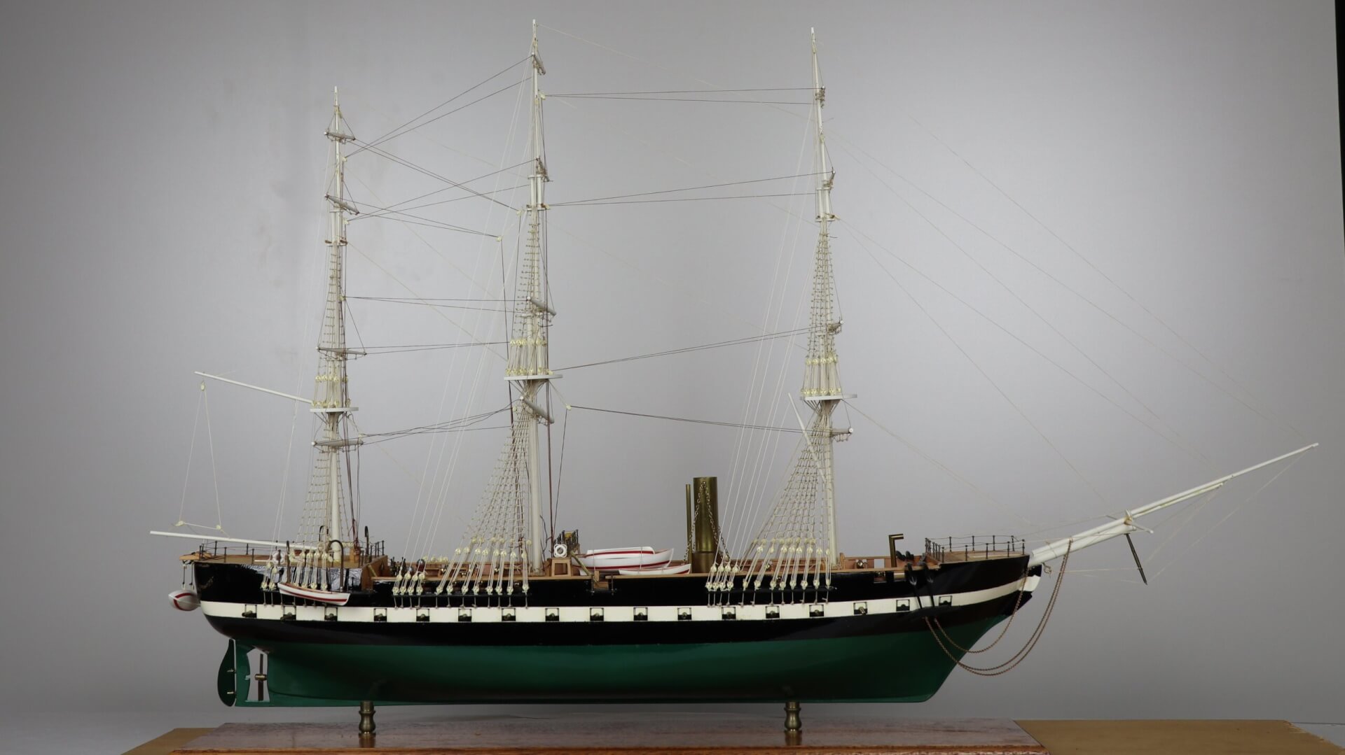 Model of a sailing ship with multiple masts, intricate rigging, and lifeboats. The ship has a black hull and a green underside.