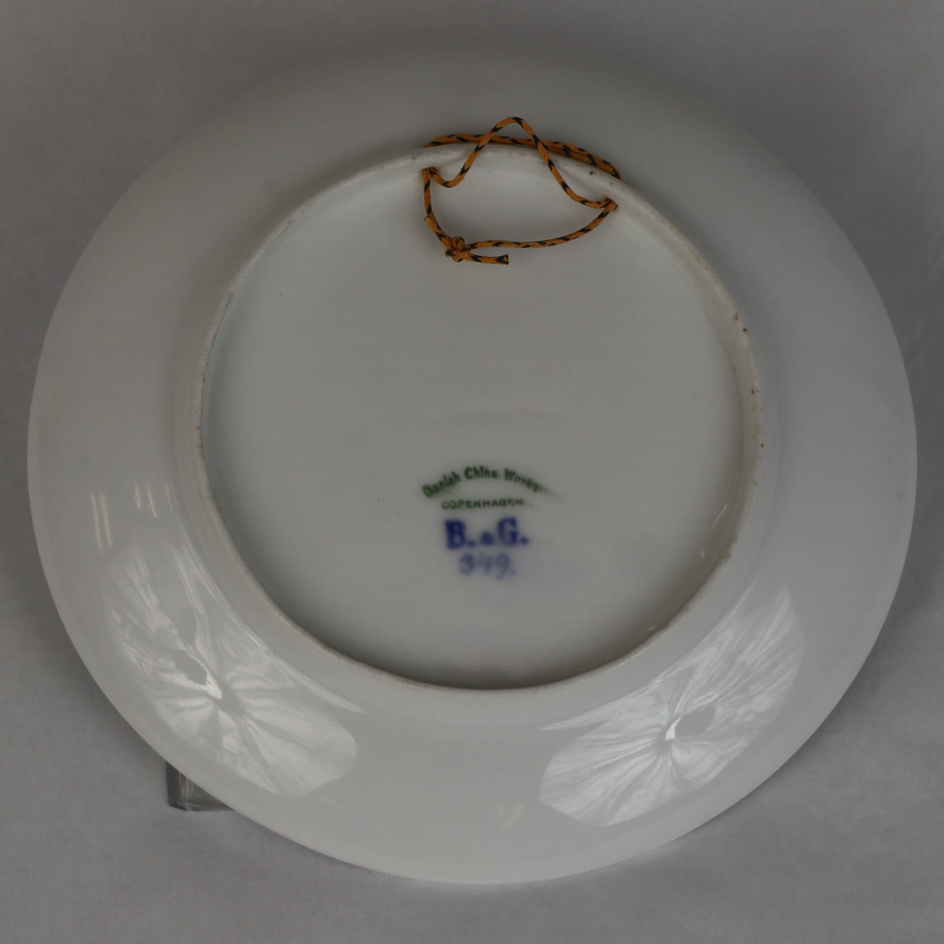 Back of a ceramic plate. An orange rope is on the top of the image. Text at the bottom reads "Danish China Works. Copenhagen. B. & G. 349"