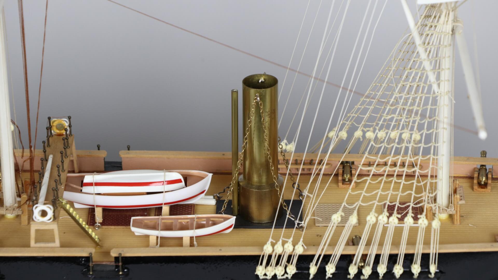 Brass chimney protruding from the deck of a model ship. To the chimney's left are white lifeboats.