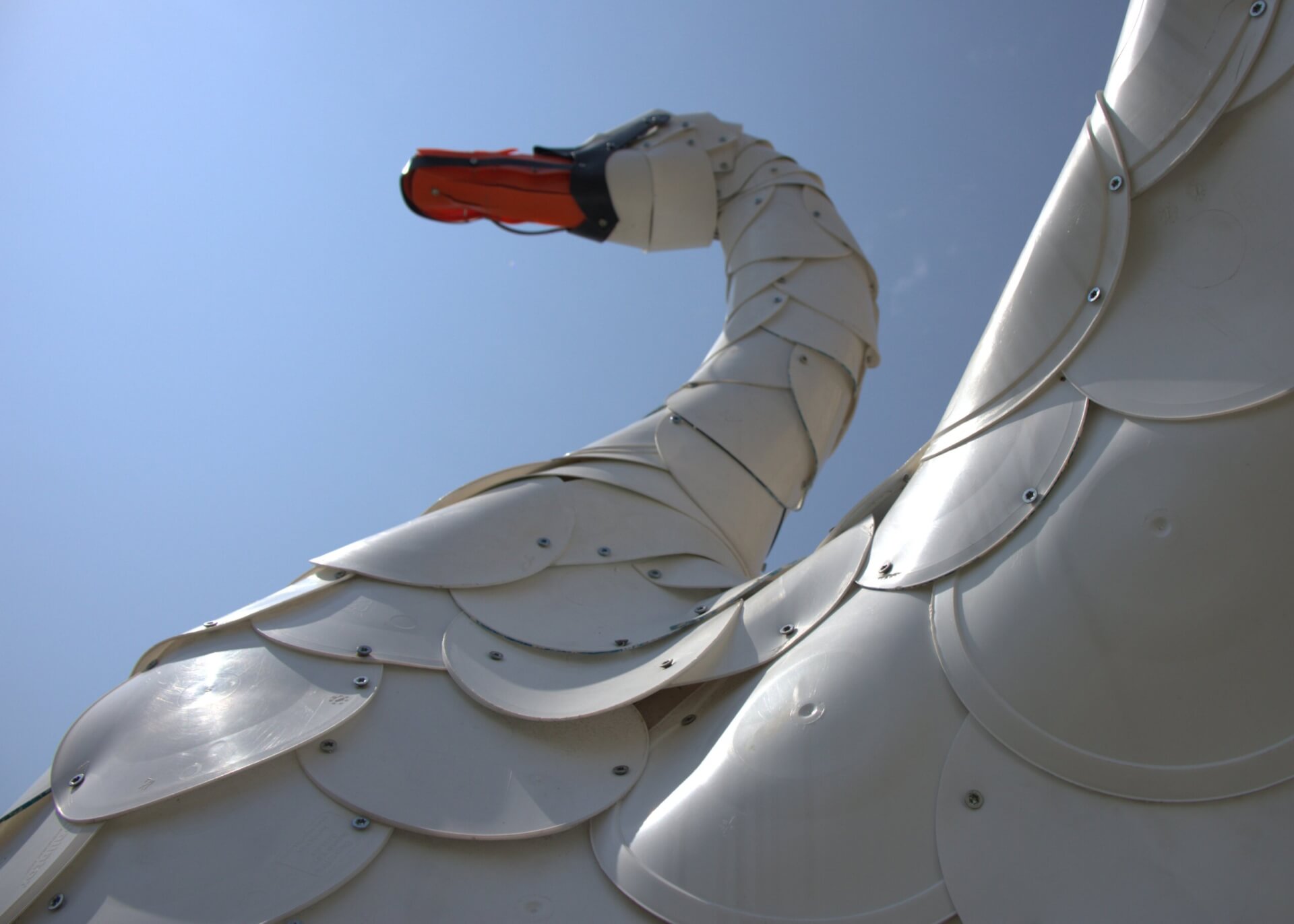 Swan sculpture made of white plastic. The swan is facing right. Blue sky is behind it.