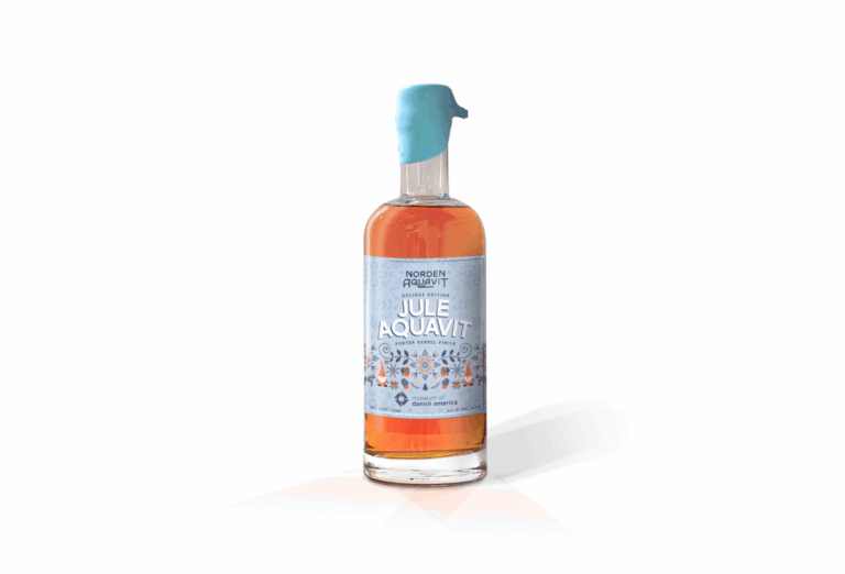The 2025 MoDA-branded Jule Aquavit. The label of the bottle is light blue and features Scandinavian elements. The liquid is amber.