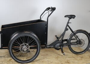 Black cargo bike. The front of the bike has a large black trunk.