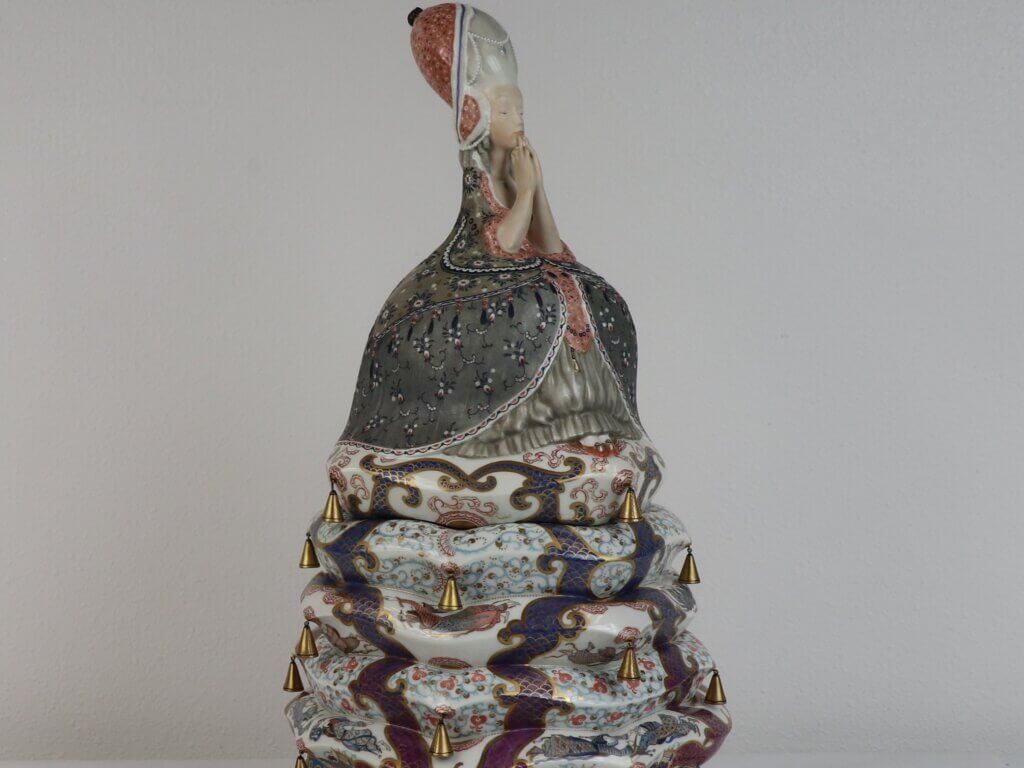 A colorful ceramic sculpture depicting a sitting woman on top of several mattresses.