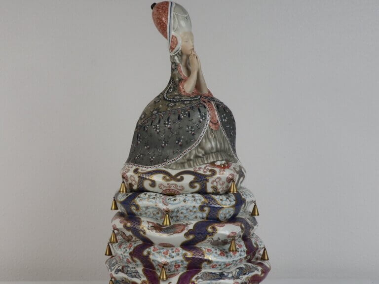 A colorful ceramic sculpture depicting a sitting woman on top of several mattresses.