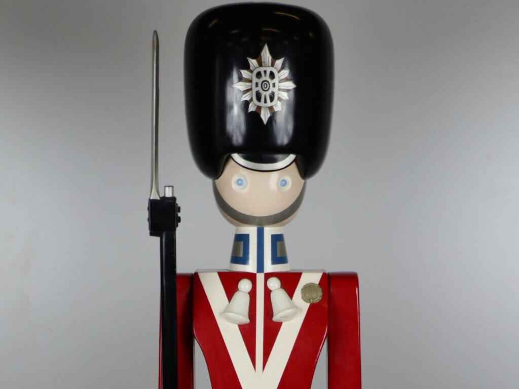 Tall wooden toy soldier with black hat and rifle, wearing a red coat with white trim.