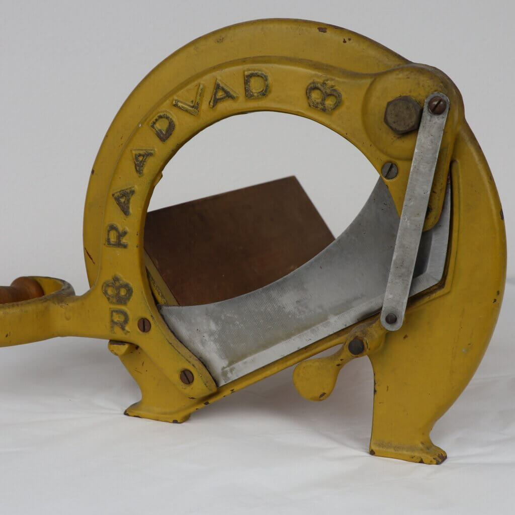Yellow metal slicer with a circular blade. It has a curved wooden handle.