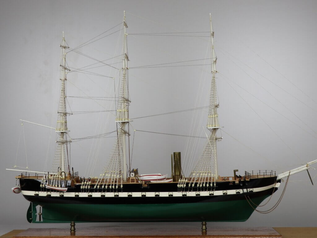 Model of a sailing ship with multiple masts, intricate rigging, and lifeboats. The ship has a black hull and a green underside.
