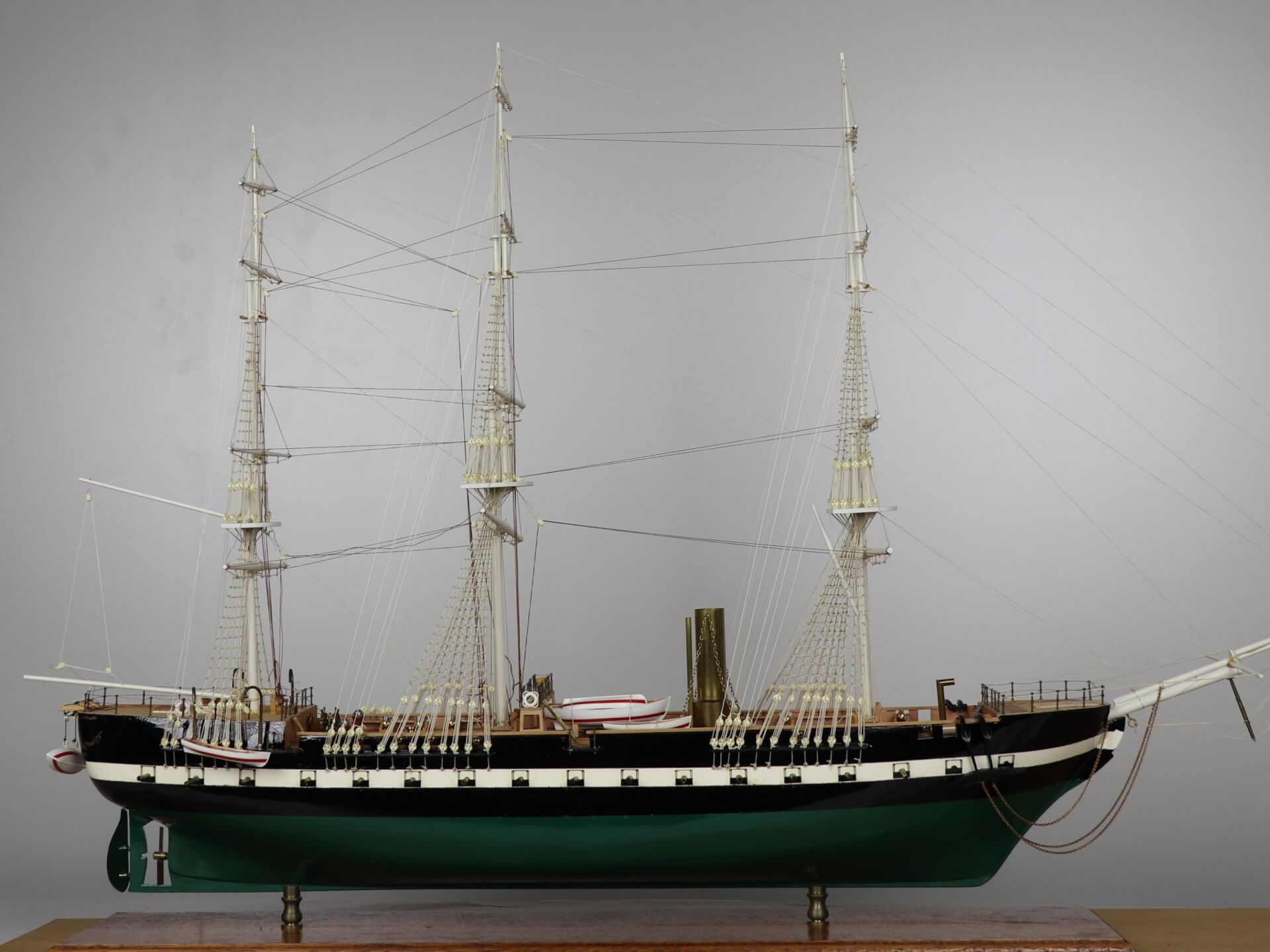 Model of a sailing ship with multiple masts, intricate rigging, and lifeboats. The ship has a black hull and a green underside.