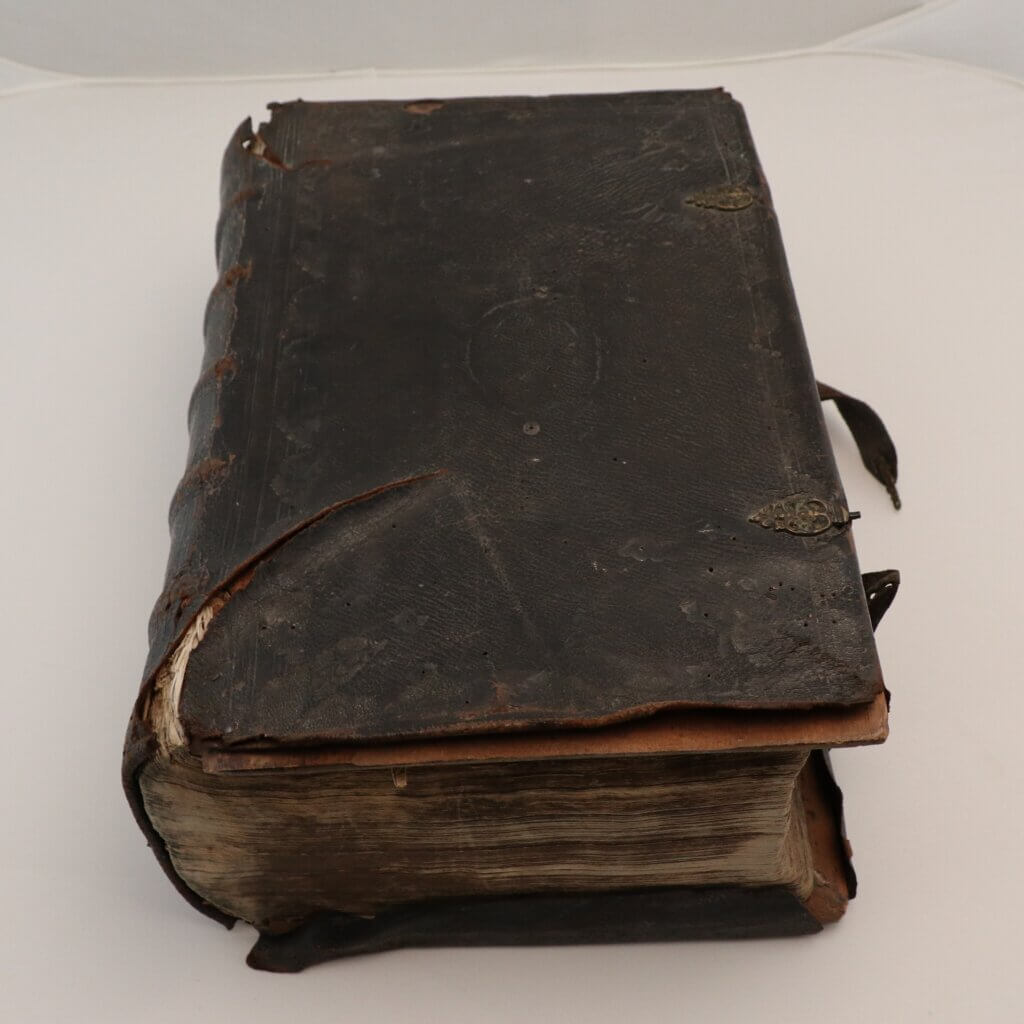 An old leatherbound book with brass clasps. THere is a large tear by the spine.