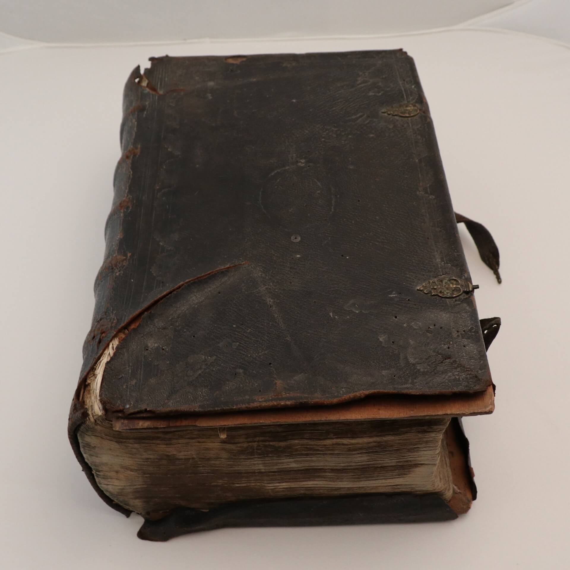 An old leatherbound book with brass clasps. THere is a large tear by the spine.