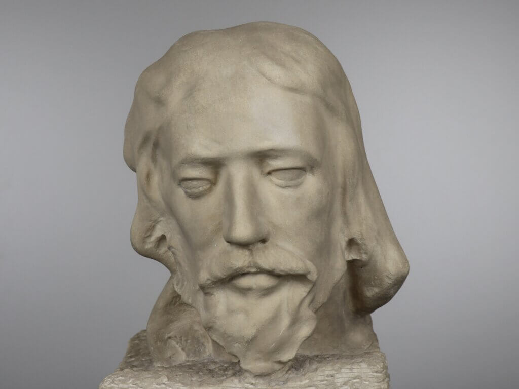 A stone bust depicting a male with long hair and a beard on a rectangular base.