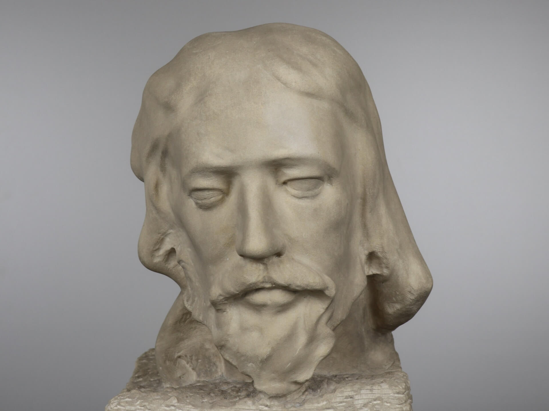 A stone bust depicting a male with long hair and a beard on a rectangular base.