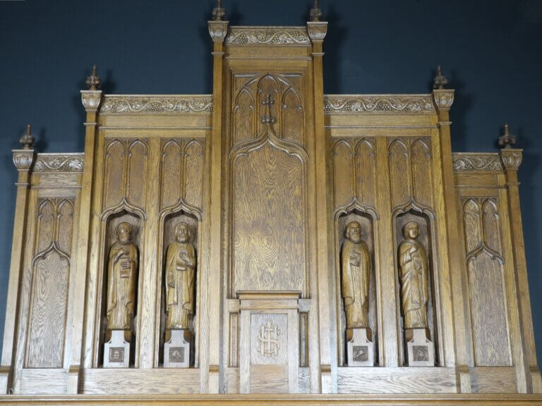 Ornate wooden altar with intricate carvings and four statues of human figures in niches.
