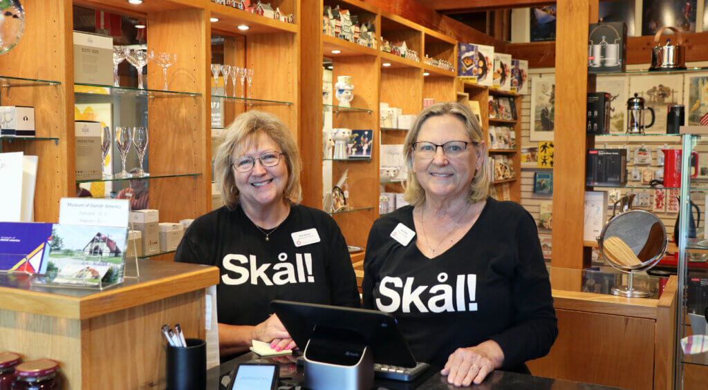 Two staff members, dressed in black long sleeve shirts emblazoned with Skål, stand behind the register at the Museum's Design Store.