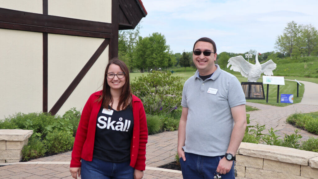 Two staff members stand before the museum. Thomas Dambo's Nordic Swan can be seen in the background.