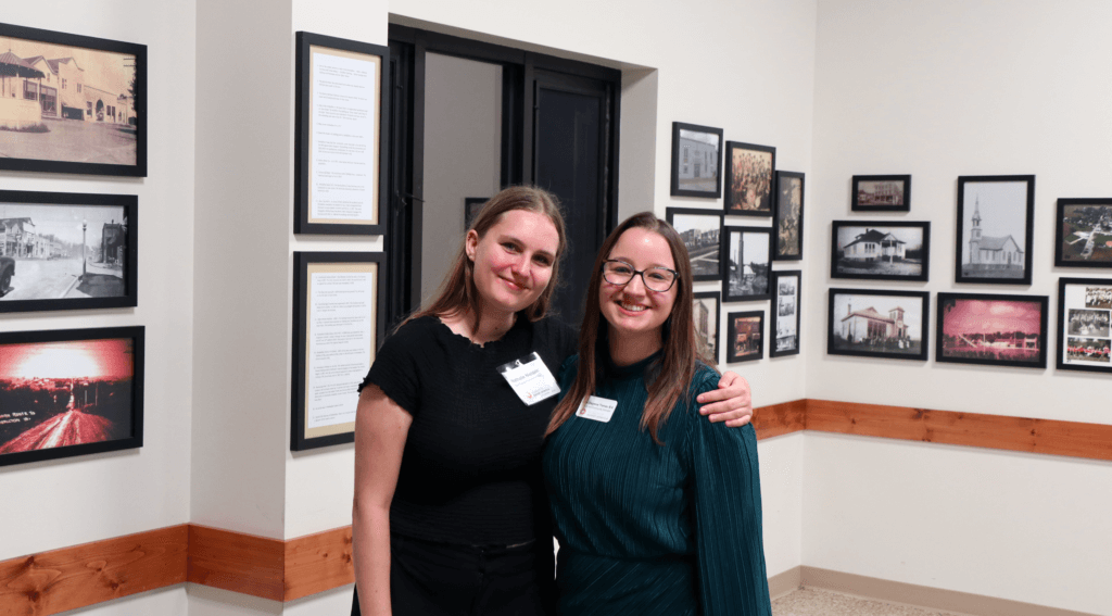 Two staff members pose for a photo with their arms around one another's shoulders at a museum function.