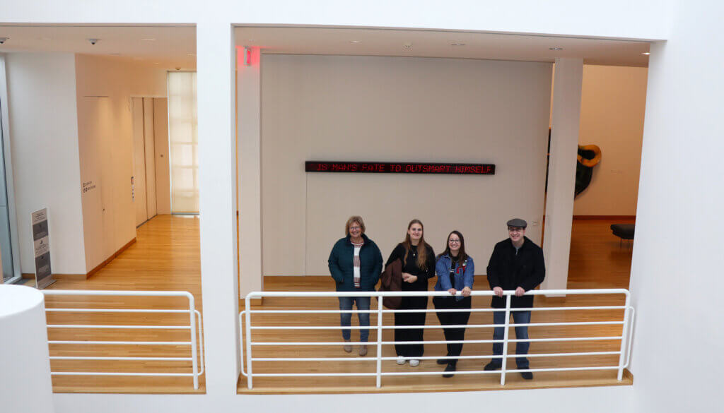 Four staff members pose alone a railing at the Des Moines Art Center during a staff outing.