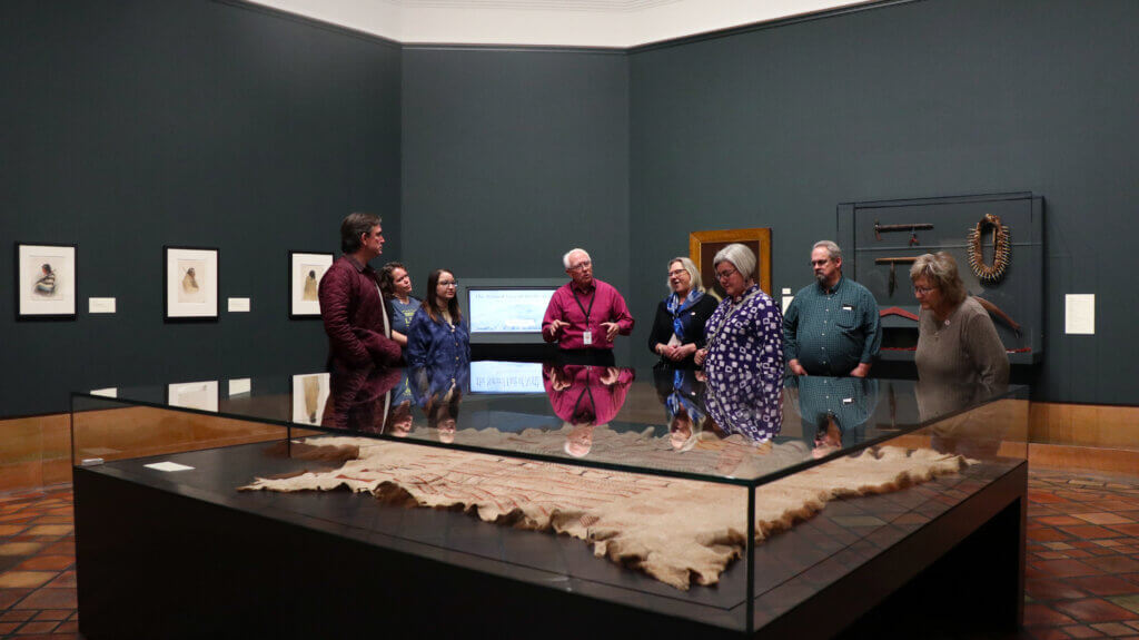Staff members receive a tour at the Joslyn Art Center. Staff stand behind a large glass display.